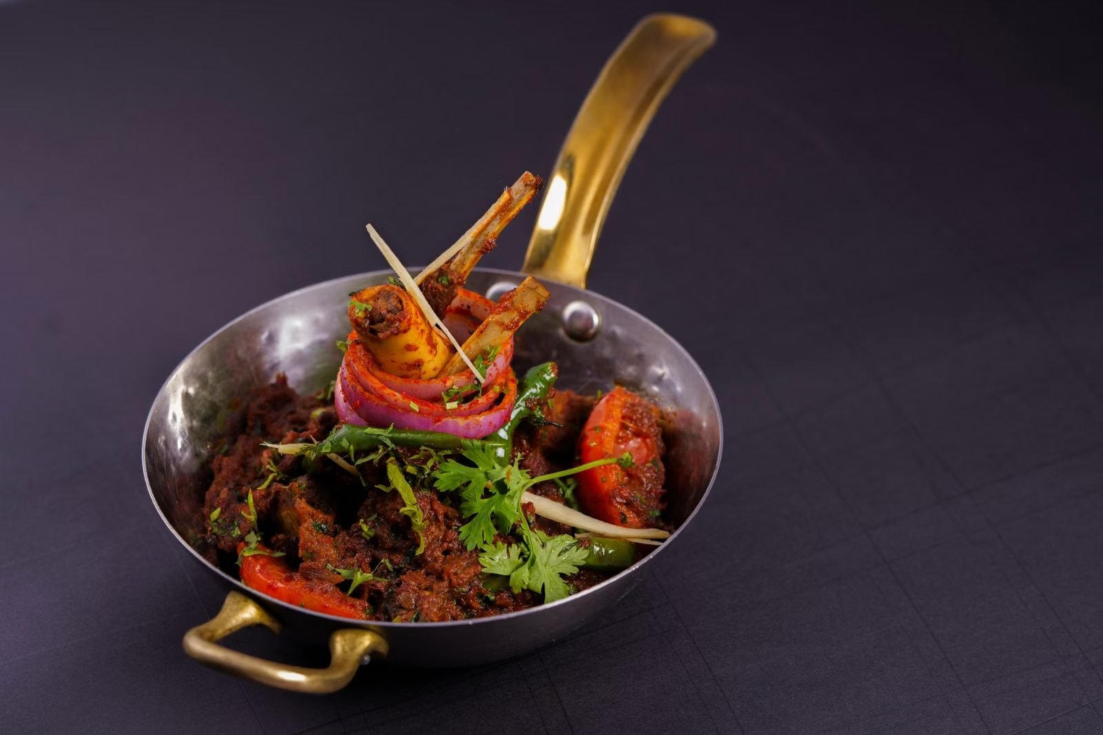 A lamb curry finished with fresh herbs in a brass serving pot