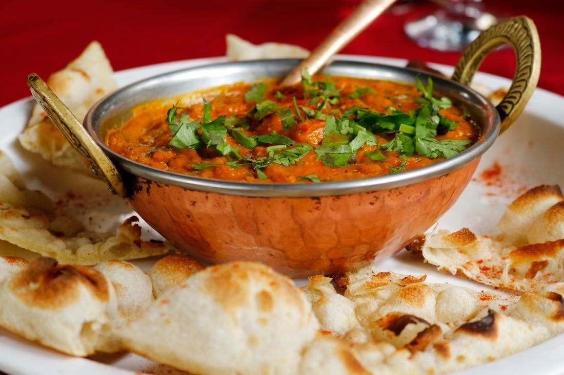 A single curry served in a copper dish alongside warm naan
